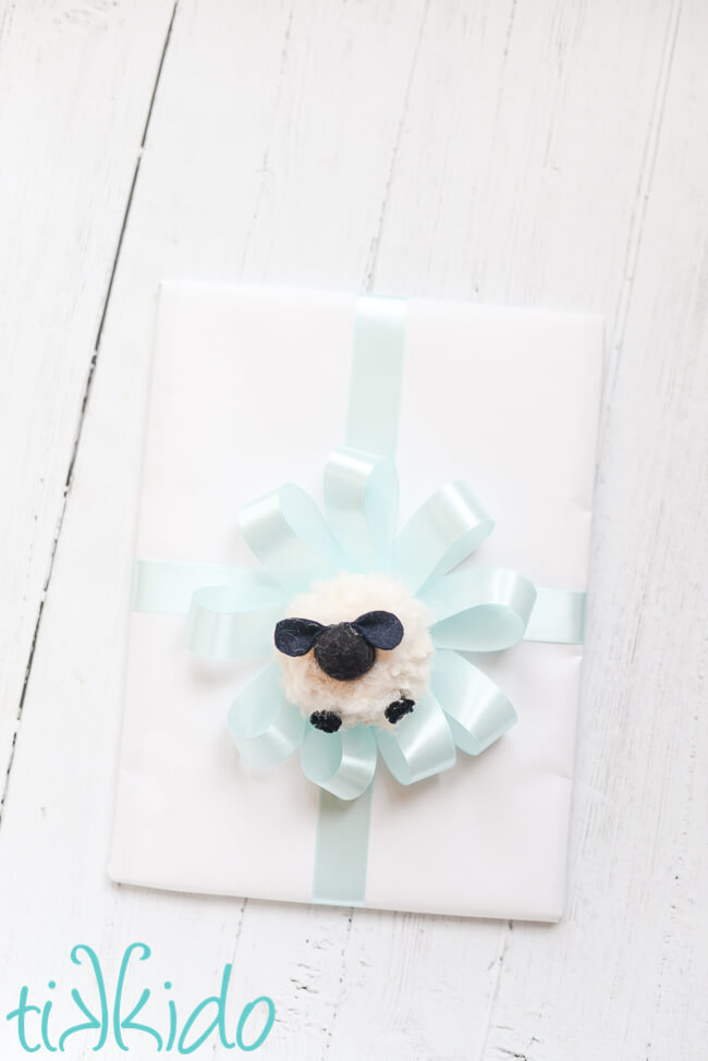 Pom Pom Sheep in the center of a bow on a baby shower gift.