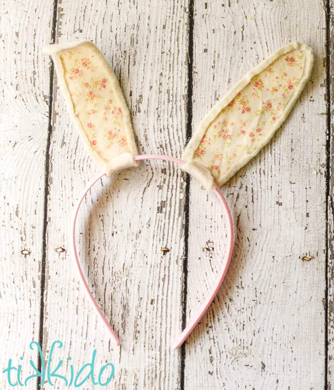 Fabric bunny ears attached to a pink headband, on a white weathered wood surface.