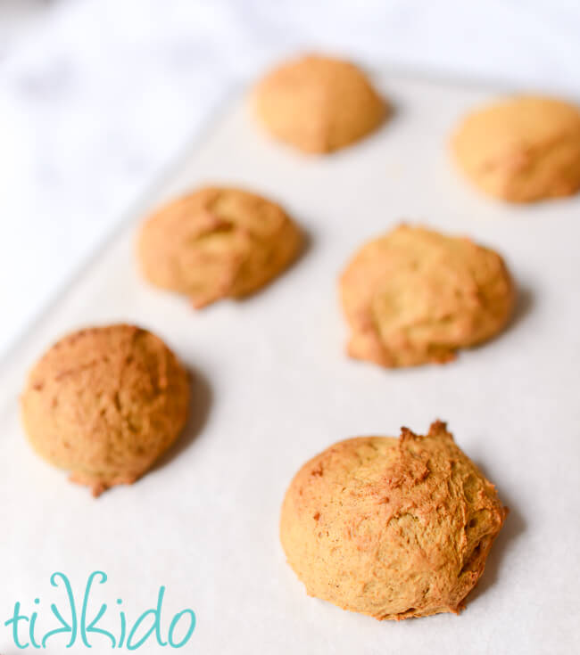 Freshly baked soft pumpkin cookies on a parchment lined cookie sheet.