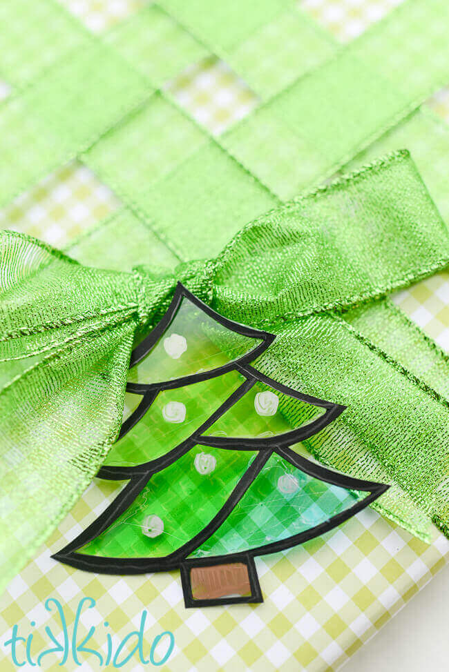 Tree shaped green faux stained glass gift tag on a present wrapped in green gingham and green ribbon. 