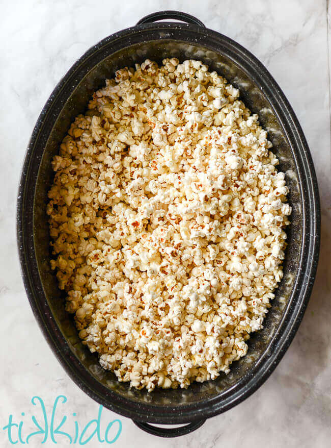 Popped popcorn in a large metal roasting pan for making homemade caramel corn.