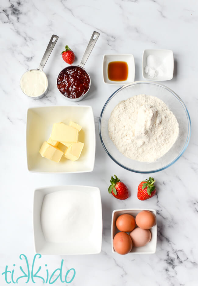 Ingredients for strawberry bread recipe on a white marble surface.