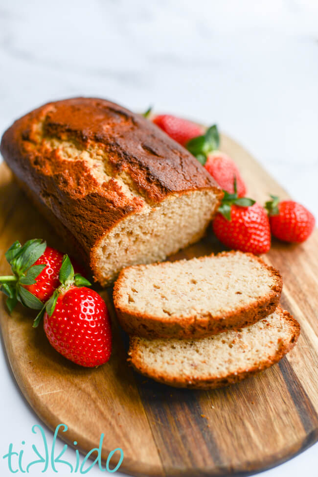 Loaf of strawberry bread with two slices cut, on a wooding cutting board, surrounded by fresh strawberries.