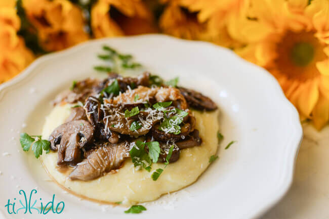 Cheesy polenta topped with oven roasted mushrooms on a white plate.