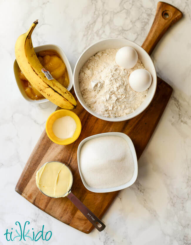 Ingredients for banana bread waffles on a wood cutting board on a white marble surface.