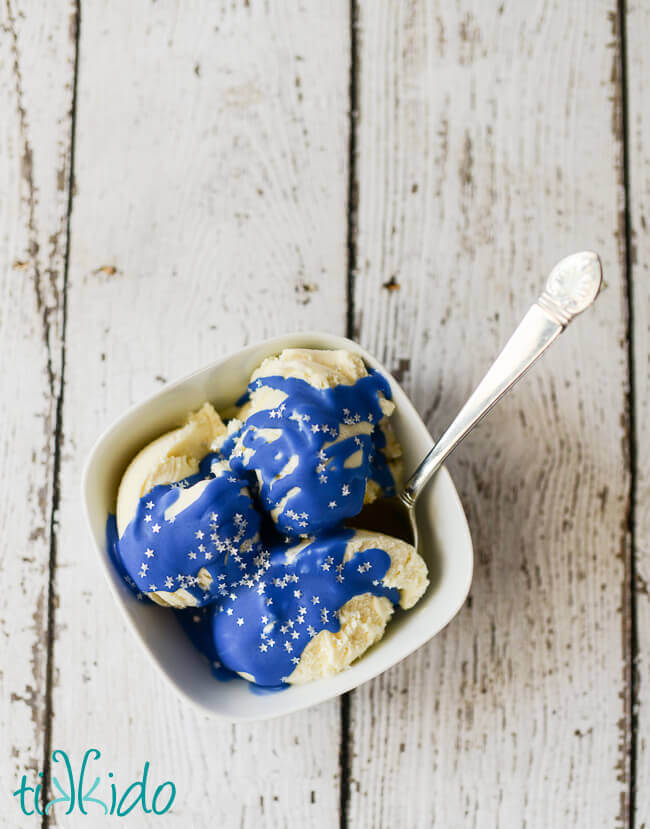 Bowl of vanilla ice cream covered in Blue Magic Shell Ice Cream Topping and silver star sprinkles.  A spoon sits in the bowl, tucked under the ice cream.