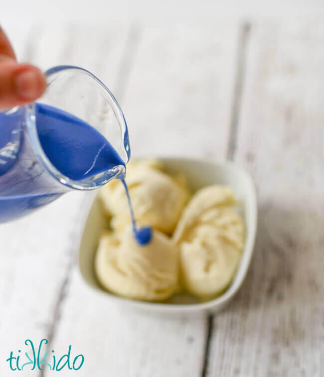 Blue Magic Shell Ice Cream Topping being poured over vanilla ice cream in a white bowl.