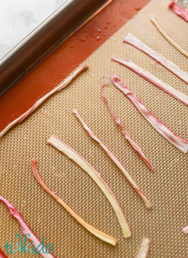 Strips of candied rhubarb on a silpat liner in a metal sheet pan.