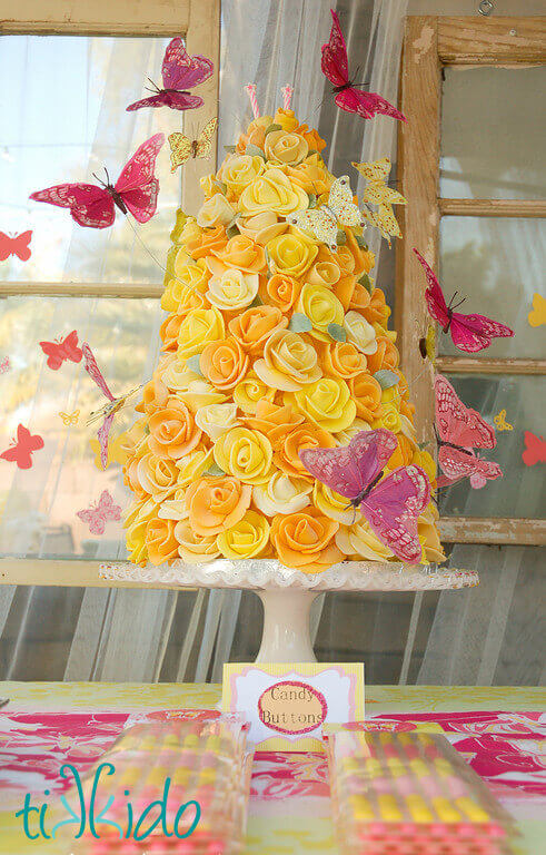 Homemade pink and yellow candy buttons in front of a pink and yellow butterfly rose tower cake.