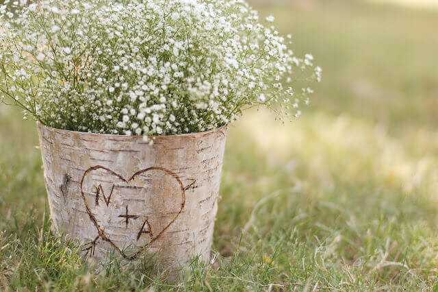 Birch bark covered zinc floral container full of Baby's Breath flowers with the letters N + A in a heart carved into the bark.