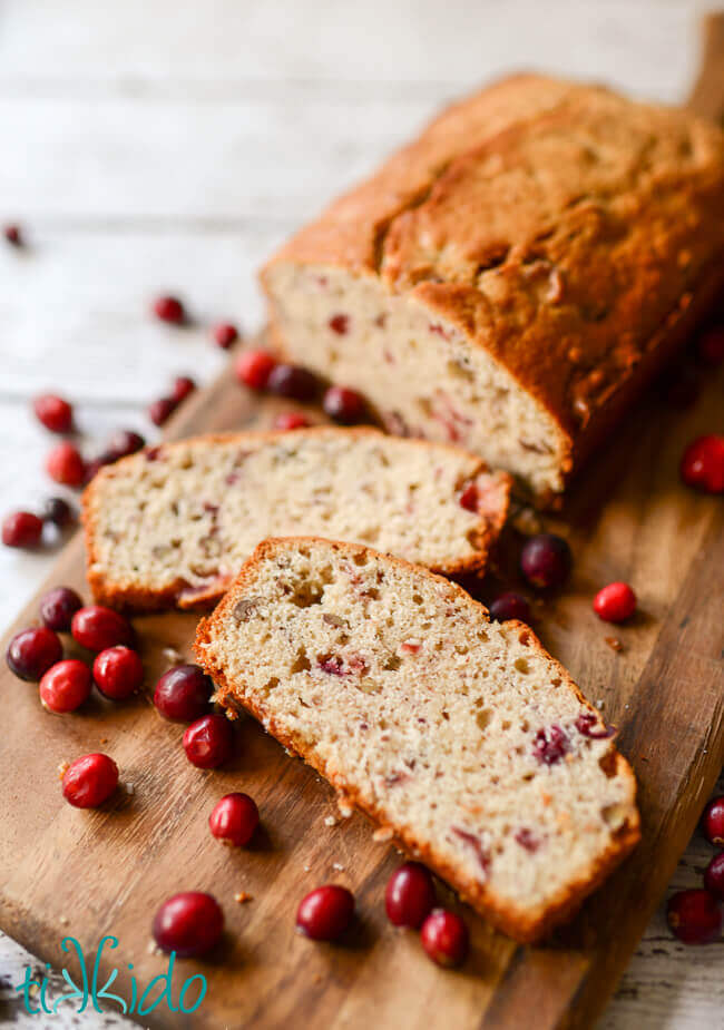 Sliced Cranberry Sauce Bread on a cutting board surrounded by cranberries.