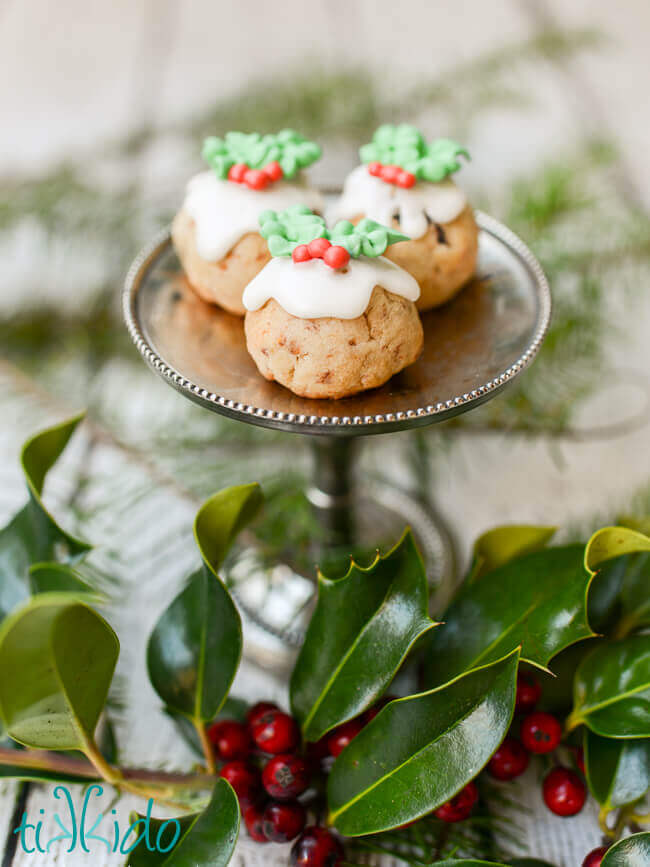 Three figgy pudding Christmas cookies that look like miniature Christmas puddings on a silver stand.