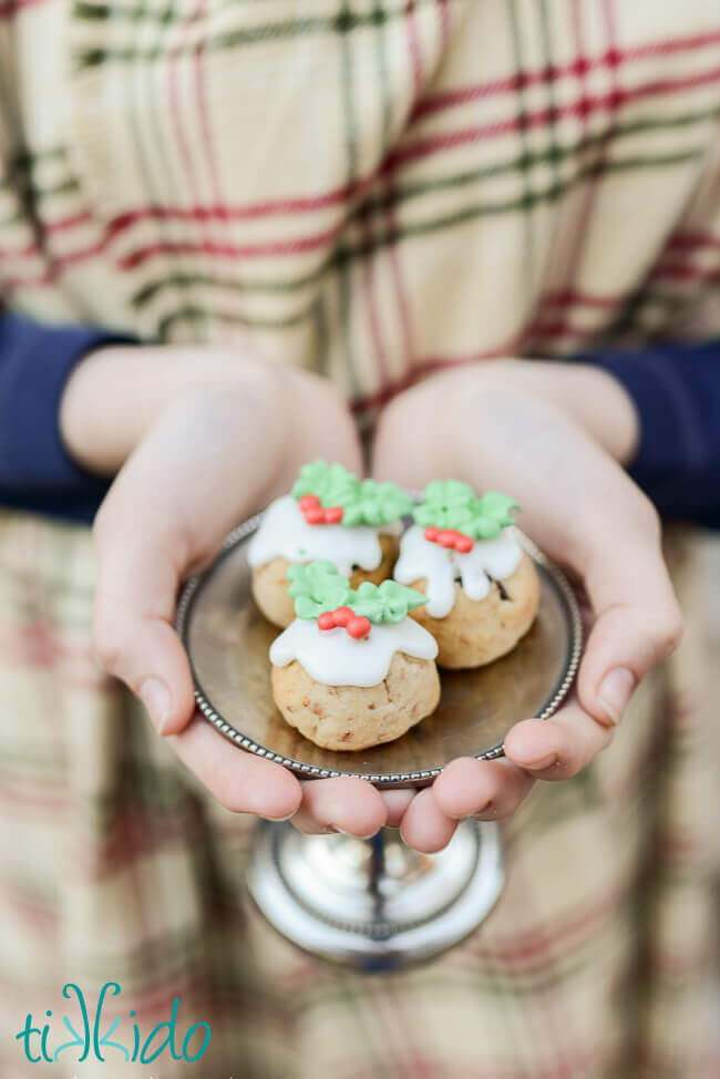 Three Figgy Pudding Cookies on a small silver tray, held in a woman's hands.