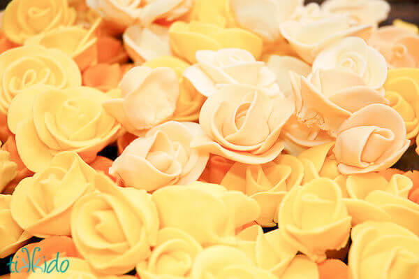 Pile of many fondant roses made in varying shades of yellow.
