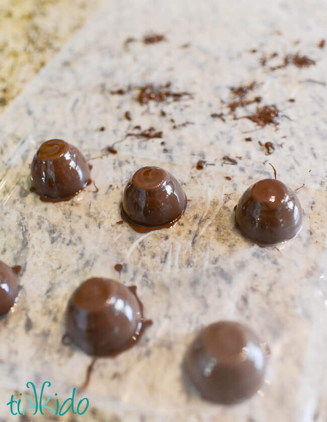 Filled chocolate candy molds coated in chocolate, and turned over on a parchment paper surface.