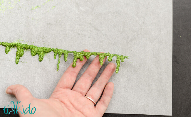 Glitter slime garland being pulled off parchment paper.