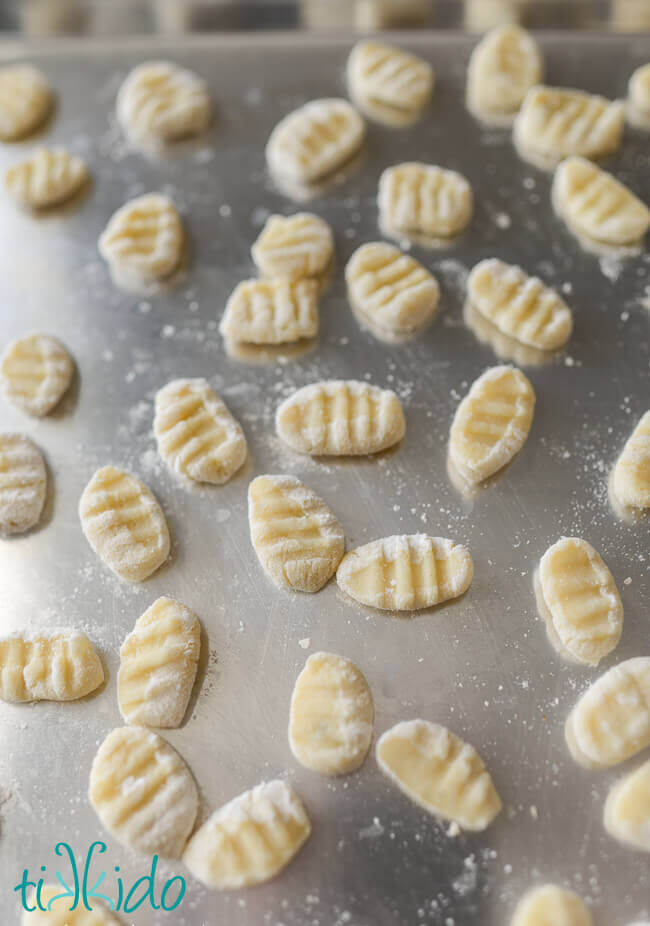 Shaped, uncooked gnocchi on a metal baking sheet.
