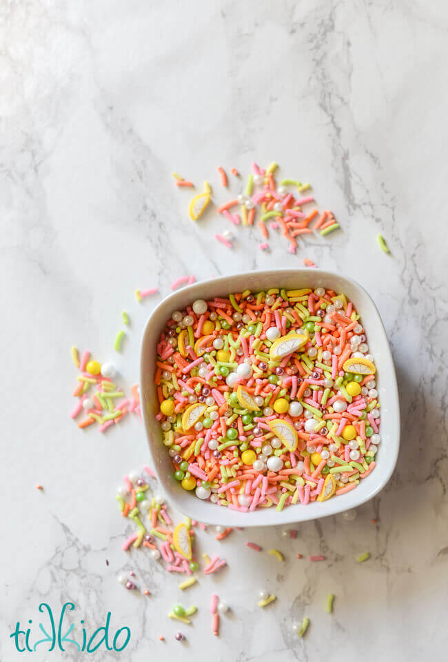 Homemade sprinkles mixed together in a white bowl on a white marble background.