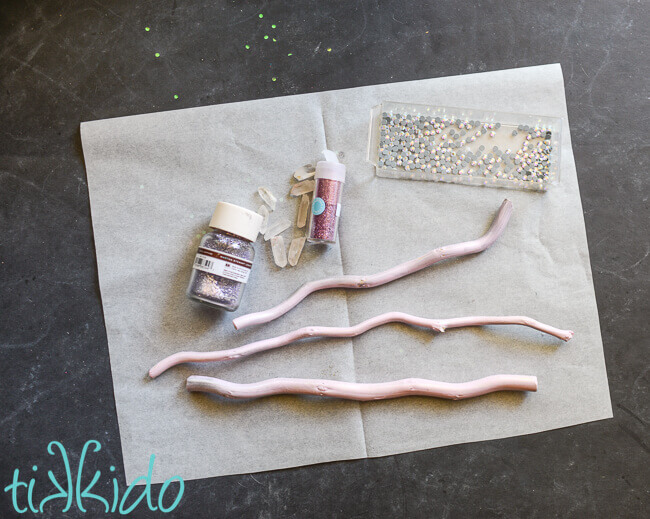 Pastel painted curly willow sticks, glitter, quartz crystals, and rhinestones on a piece of parchment paper.