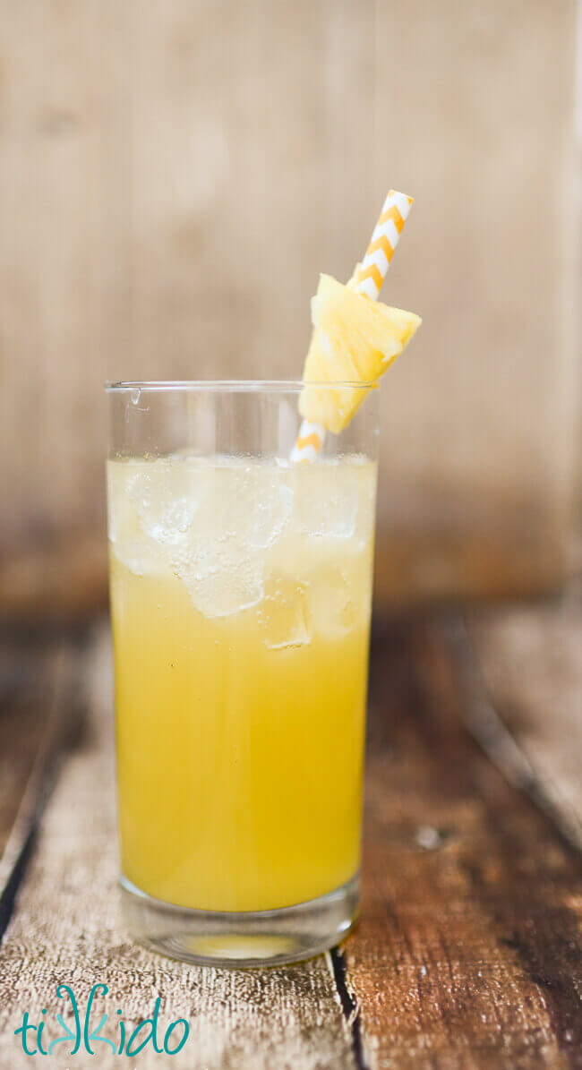 Pineapple and coconut rum summer cocktail in a tall glass, with a yellow and white chevron striped paper straw and a chunk of fresh pineapple.
