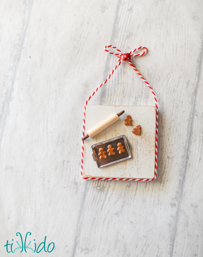Christmas ornament that looks like a miniature baking scene with a tiny pan, rolling pin, and gingerbread cookies.