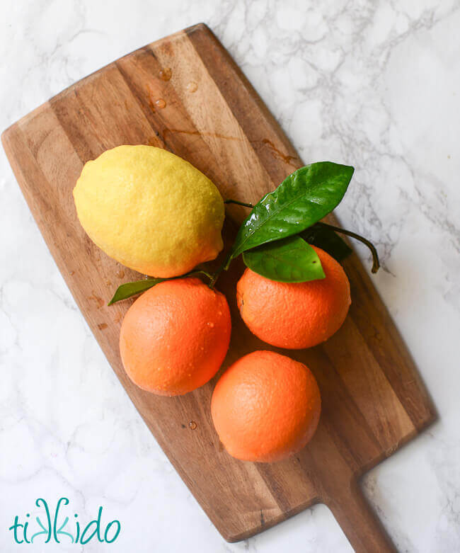 Fresh oranges and a lemon on a wooden cutting board.