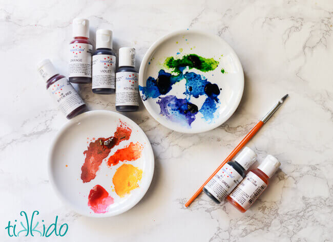 Collection of gel food colorings and two small white plates used as paint palettes