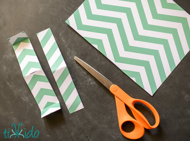 Paper noisemaker being made by cutting a strip of green and white striped paper.