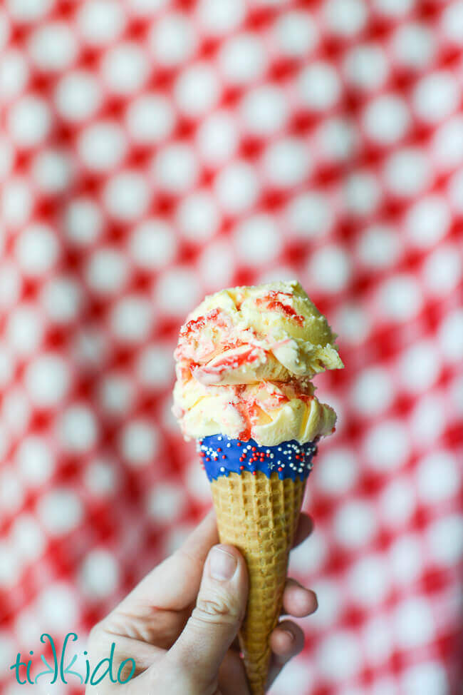 Red, white, and blue ice cream cones with chocolate and sprinkles filled with two scoops of ice cream on a red checkered background.