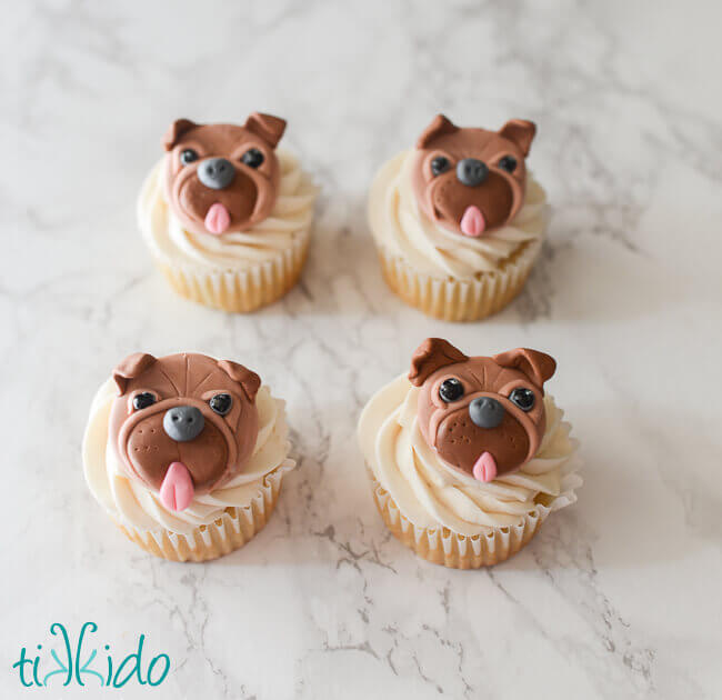 Four cupcakes decorated with gum paste pugs