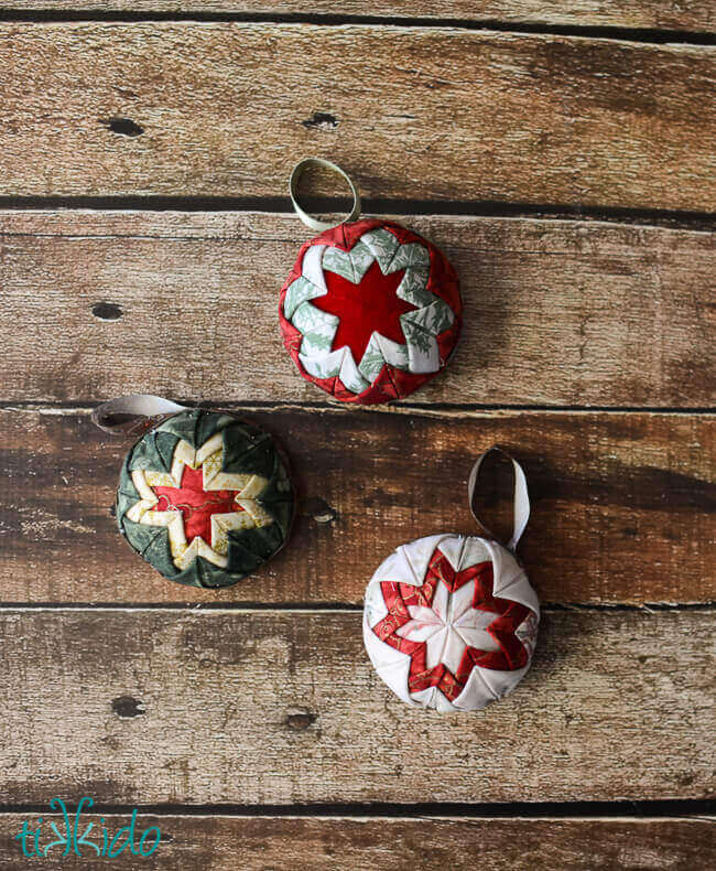 three finished no sew quilted star Christmas ornaments on a wooden background.