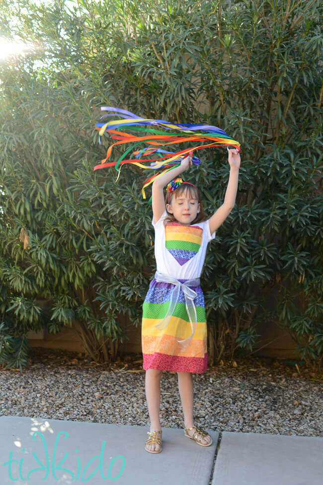 Little girl playing with rainbow ribbon toys, wearing a rainbow outfit.