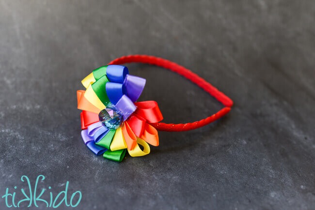 Rainbow DIY headband made with satin ribbon on a black chalkboard background.
