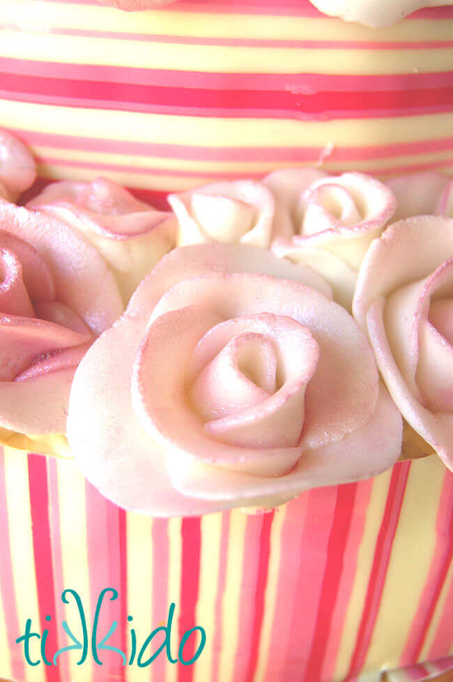Rolled buttercream roses on a pink and white striped cake.