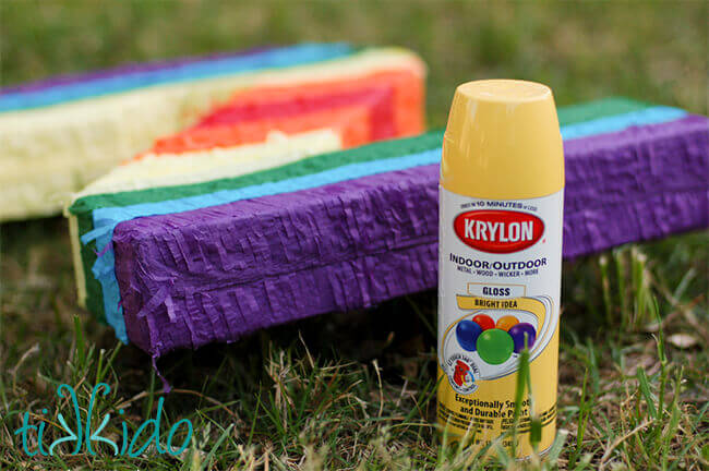 Store bought rainbow piñata next to a can of yellow spray paint on grass.