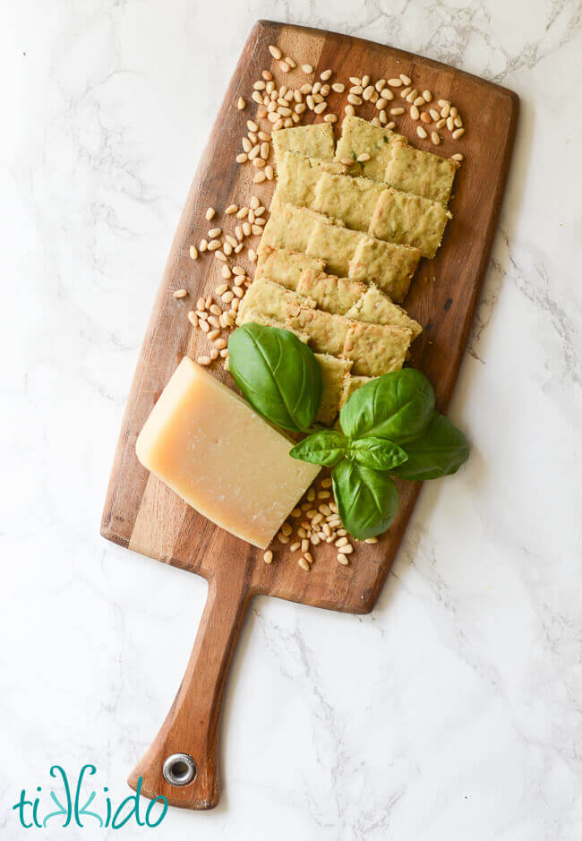 Savory Pesto Shortbread surrounded by parmesan cheese, fresh basil, and pine nuts on a wooden cutting board.