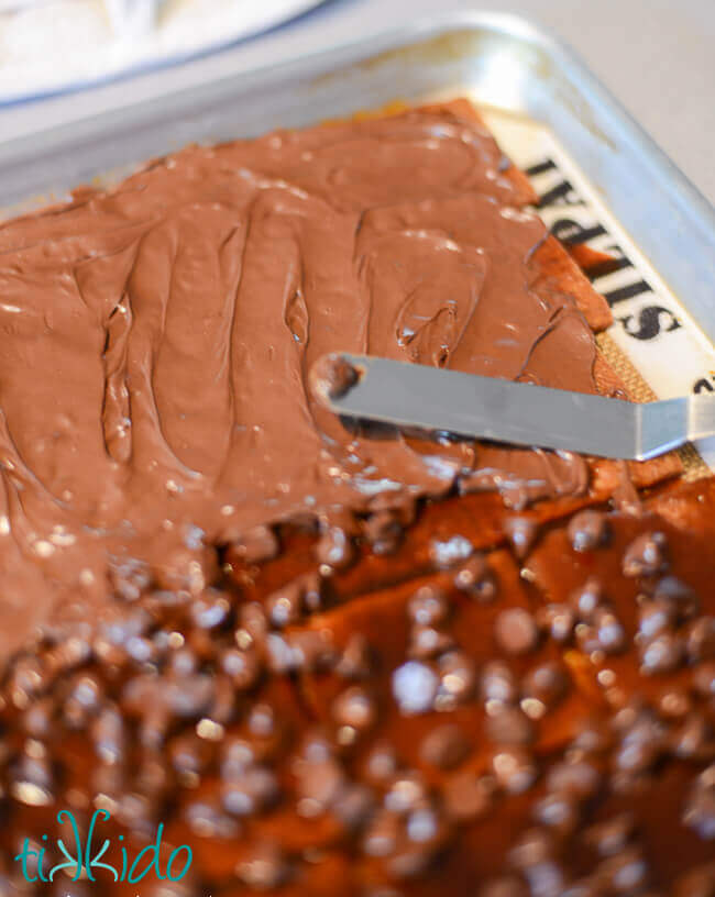 Melted chocolate chips being spread with an offset spatula on the S'mores Toffee graham cracker base.