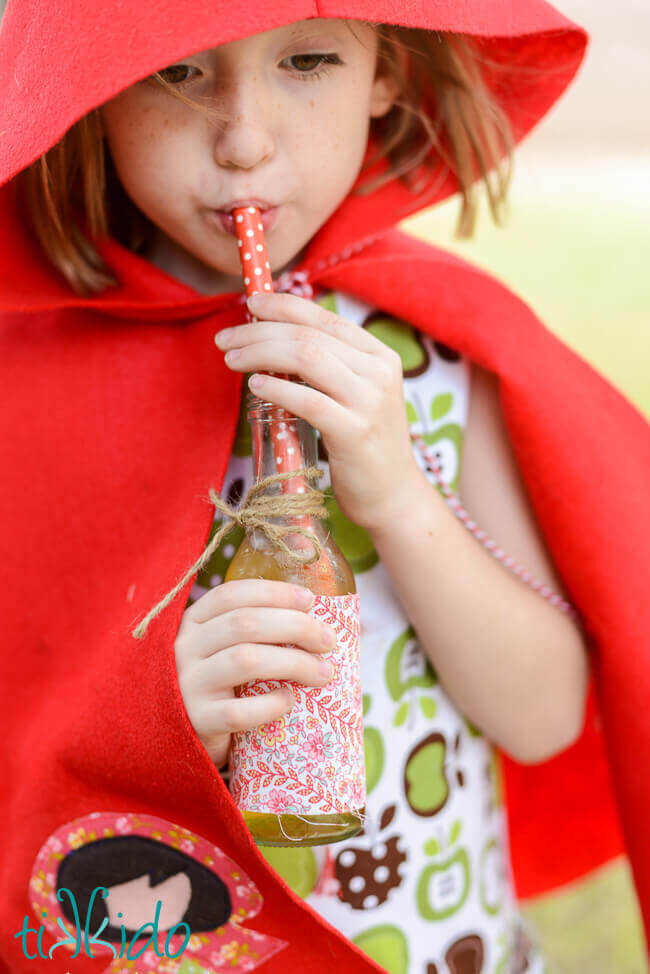 Little girl in a red riding hood cape drinking Sparkling Apple Cider