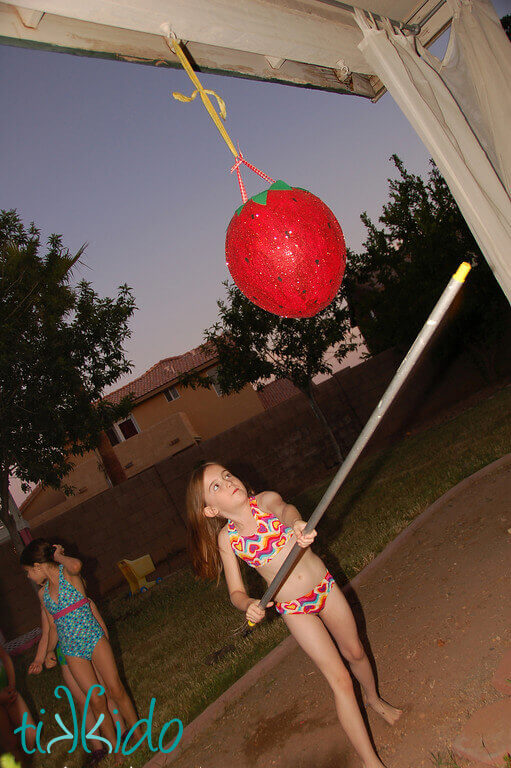 Little girl swinging at the strawberry piñata at the Strawberry Picnic birthday.