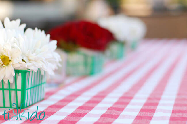 Red and white flower arrangements in green plastic strawberry baskets at the Strawberry Picnic birthday.