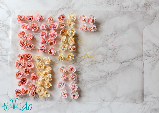 Collection of pink and white gum paste roses drying on waxed paper on a white marble background.