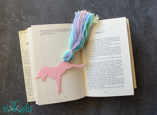 Unicorn bookmark with a yarn tassel tail on an open book.