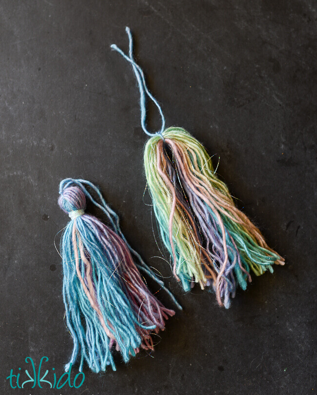 Two yarn tassels made with pastel rainbow yarn being tied into tassel shapes.
