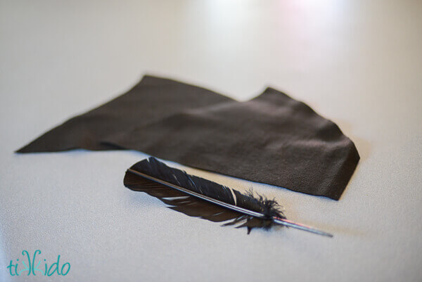 Felt and feather pieces for an all black Peter Pan hat on a grey surface.