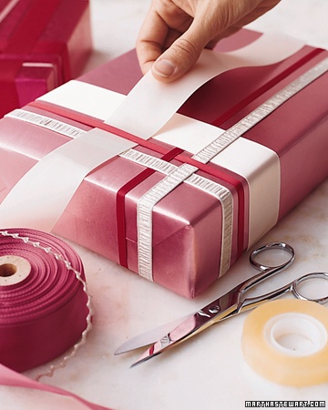 Plain pink gift being embellished with woven ribbon of various widths.
