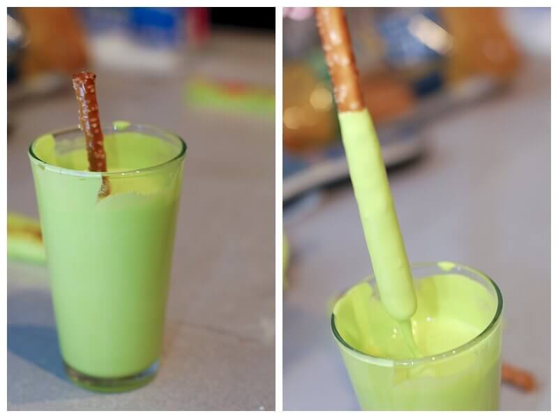 Pretzels with icing being made by dipping pretzel sticks into a glass of thin royal icing.