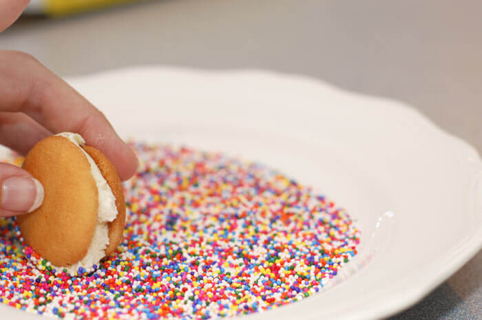 Vanilla ice cream sandwiched between two Nilla wafers, edge of the ice cream being rolled in rainbow sprinkles.
