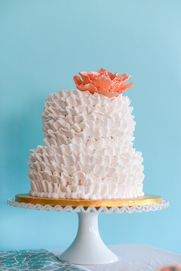 Two tier white ruffled buttercream cake topped with a peach gum paste peony