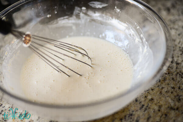Apple fritter batter being whisked together in a clear bowl.