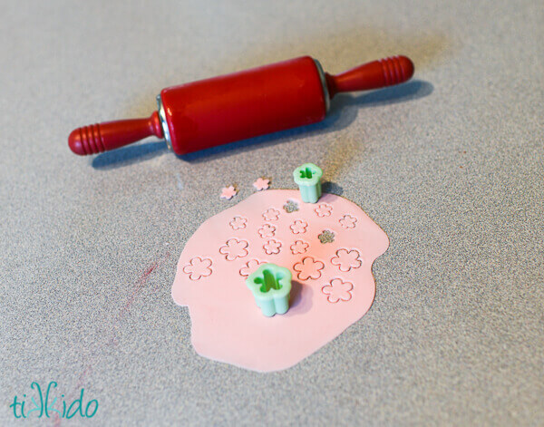 pink gum paste rolled out with a small red rolling pin, with small flower shapes being cut out using gum paste cutters.